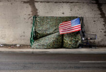 Audit Stunner: Camps Bounce Back A makeshift shelter draped with an American flag next to a shopping cart on a city street