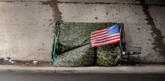 A makeshift shelter draped with an American flag next to a shopping cart on a city street