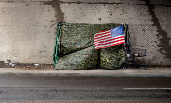 A makeshift shelter draped with an American flag next to a shopping cart on a city street