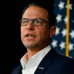 Results-First Governor Sparks Democratic Brawl A man in a suit speaking at a podium with an American flag in the background