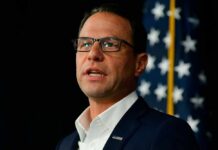 Results-First Governor Sparks Democratic Brawl A man in a suit speaking at a podium with an American flag in the background