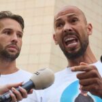 Online Empire Meets Handcuffs in Miami Two men speak into microphones during an outdoor press conference