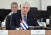 Bank Shock: Cuba Crackdown Goes Global Cuban official speaking at a conference with a flag in front