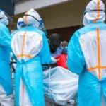 Ebola Jumps Borders — WHO Slams Alarm Medical workers in PPE assist a patient on a stretcher outdoors