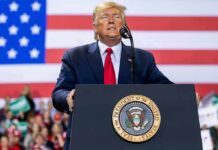 person speaking at a podium with U.S. flag backdrop