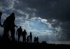 Silhouettes of people walking under dramatic cloudy sky