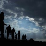Silhouettes of people walking under dramatic cloudy sky