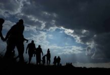 Silhouettes of people walking under dramatic cloudy sky