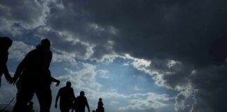 Silhouettes of people walking under dramatic cloudy sky