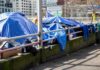 Bass Plan Backfires? Residents Hire Enforcers Tents covered with blue tarps along a city sidewalk