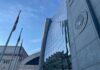 Glass-fronted government building with seal and flagpoles