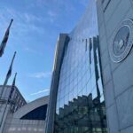 Glass-fronted government building with seal and flagpoles
