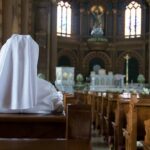 Person in white habit seated in a church pew facing the altar