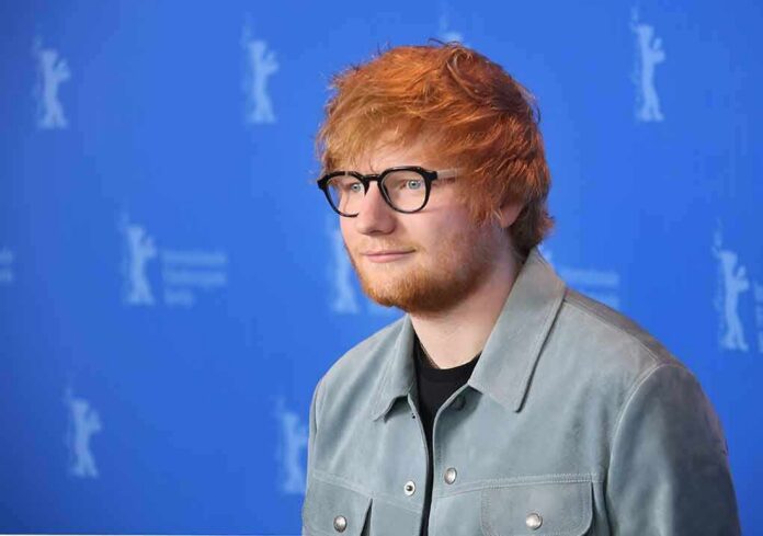 Ed Sheeran posing at a photo call against a blue backdrop