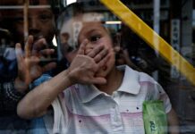 child behind a window raises hand to face