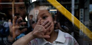 child behind a window raises hand to face