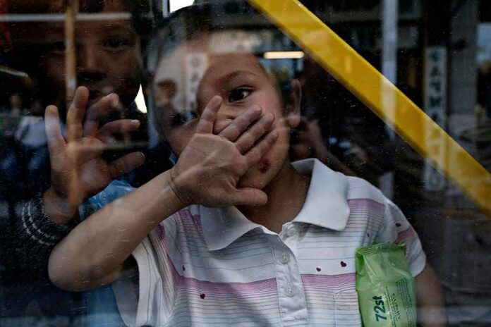 shutterstock_1090186736 child behind a window raises hand to face