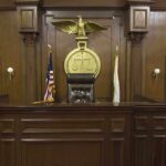 Courtroom Shock: ‘Woman’ Redefined Statewide Interior of a courtroom featuring a judges bench and American flag