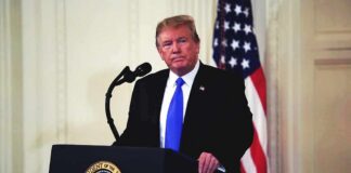 man at podium with microphone and US flag