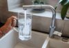 Hand holding a glass pitcher under a running kitchen faucet