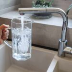 Hand holding a glass pitcher under a running kitchen faucet