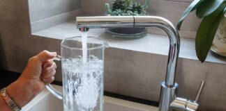 Hand holding a glass pitcher under a running kitchen faucet