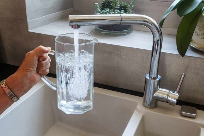 Hand holding a glass pitcher under a running kitchen faucet