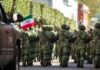Soldiers in green camouflage march carrying rifles and a Mexican flag
