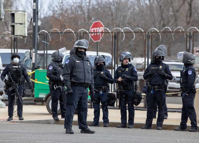 Group of police officers in riot gear standing on a street; Brian Folkerts present