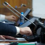 Iran Strikes Fallout Triggers House Revolt Person pressing a button on a conference microphone panel