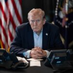 Donald Trump seated at a table between two desk phones