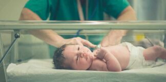 Newborn baby in hospital bassinet being cared for by nurse