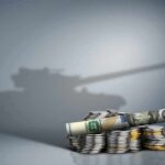 Stacked coins and rolled banknote with tank shadow in background