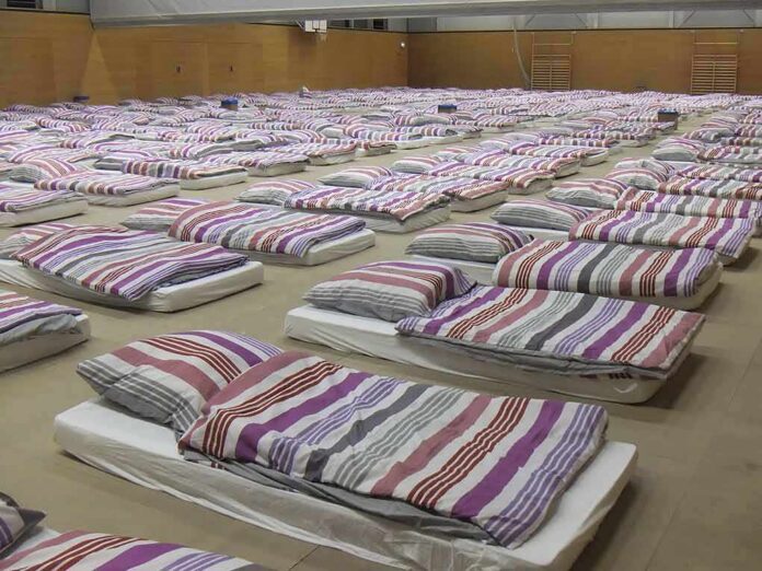 rows of mattresses with striped bedding in a large hall