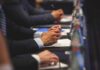 Hands of people in suits taking notes at a conference table