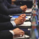 Canada’s MAID Pause Sparks Explosive Backlash Hands of people in suits taking notes at a conference table
