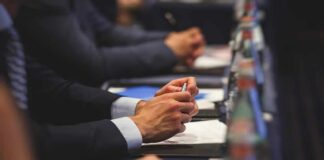 Hands of people in suits taking notes at a conference table