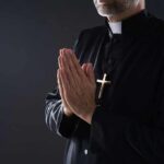 Clergyman in black robe praying with hands together