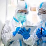 Two healthcare workers in full PPE reviewing a clipboard