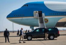 Security detail near blue and white aircraft with staircase and SUV