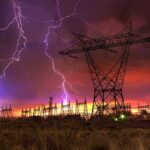 Lightning strikes illuminate a power station against a colorful sunset sky